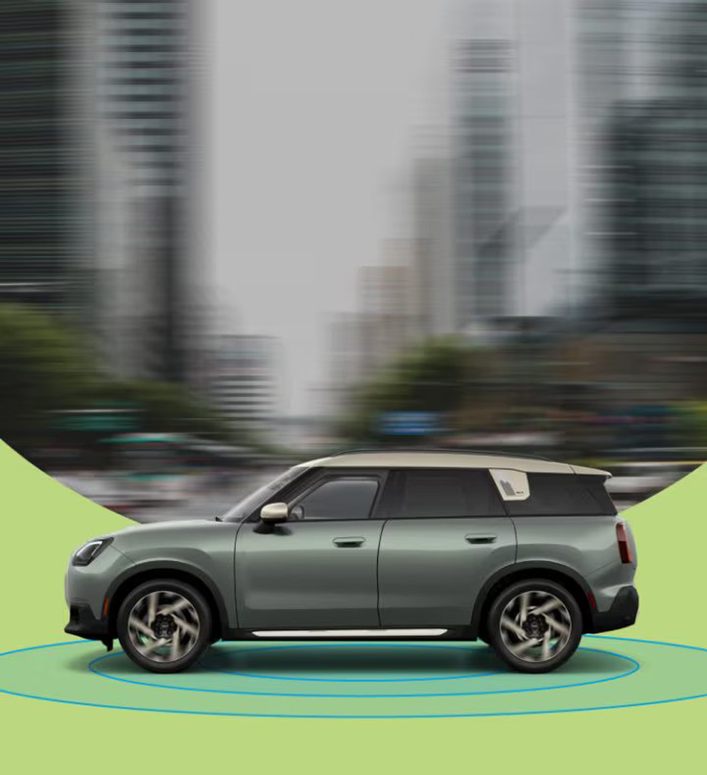 The side-view of a 2025 MINI Countryman S ALL4 with a blurred city street in the background and blue rings beneath it.